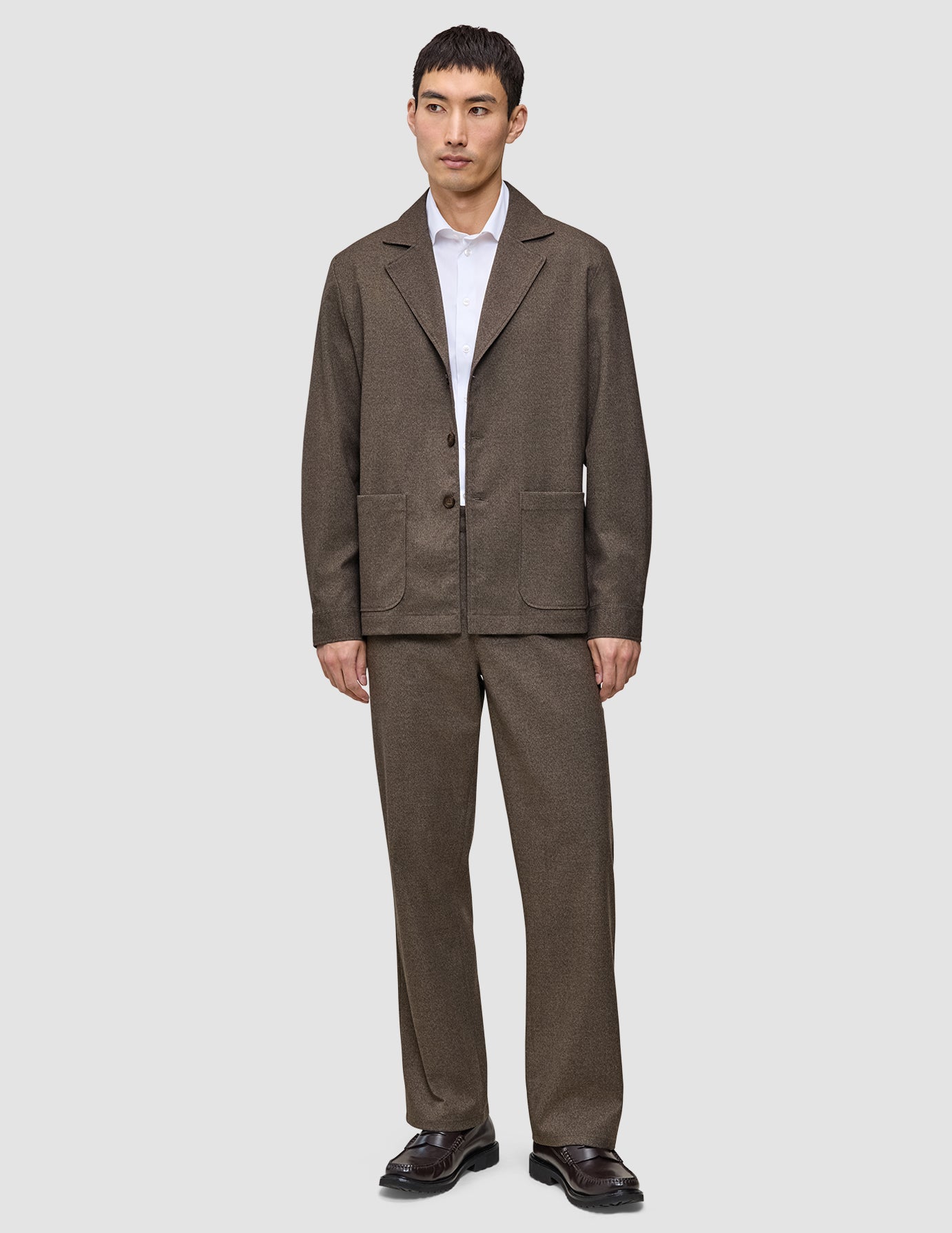 En mand iført en mørkbeige overshirt fra Atelier, en hvid skjorte med knapper, matchende bukser og mørke læderloafers.